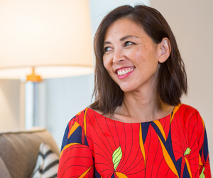 Woman sat down with dark hair and red top smiling.